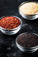 Black, white and red quinoa in bowls, raw quinoa groats set on gray kitchen table, copy space, selective focus