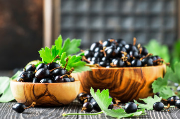 Fresh black currants in wooden bowls, on black kitchen table background, copy space, selective focus