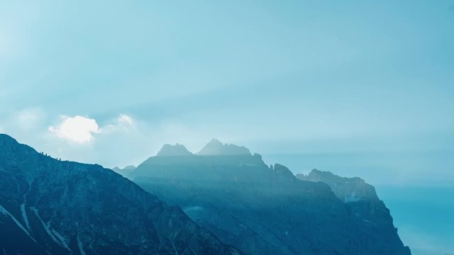 Early morning timelapse video of sunrise over the Italian Dolomite Alps. With beautiful sun rays and some fogy clouds over them. Shot during sunny summer day.