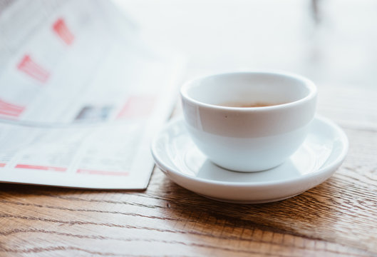 Still life image of cup of black coffee with fresh sport newspaper on the wooden table next to big coffee shop window.