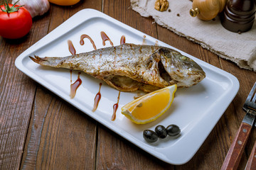 Dorado on grill on white plate on wooden table