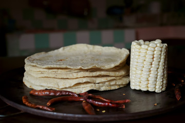 En la mesa hay muchas tortillas de maíz algunos pedazos de elote y chiles picantes.