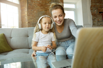 Female caucasian teacher and little girl, or mom and daughter. Homeschooling. Sitting on the sofa and using laptop for knowledges getting while lesson is. Education, school, studying concept.