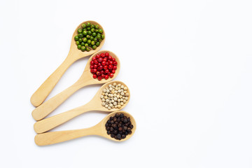 Green, red white and black peppercorns with wooden spoon on white