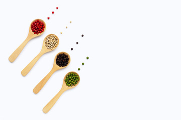 Green, red white and black peppercorns with wooden spoon on white