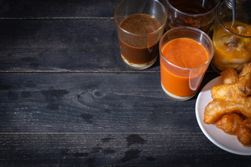 Traditional Thai hot tea with milk on the wood table there are Traditional Thai hot coffee, deep-fried doughstick (patongko), hot tea, Kettle and soft-boiled egg plated around.