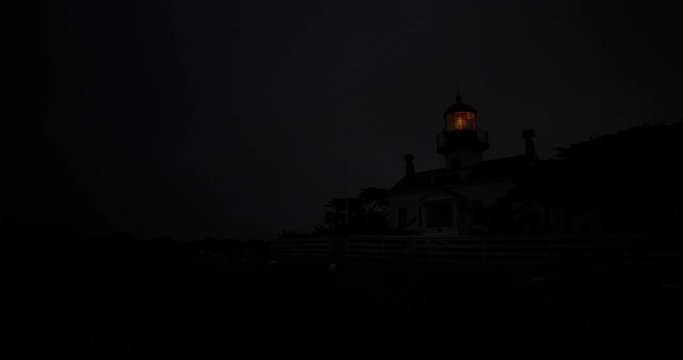 A Lighthouse Lantern Glows Through The Fog On A Dark Night