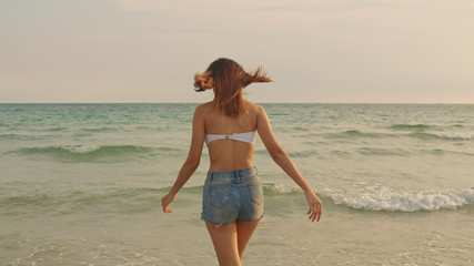 Asian woman walking on sand beach. Young happy female in bikini relax and fun walking near tropical sea when sunset while holiday, vacation, summer trip concept.