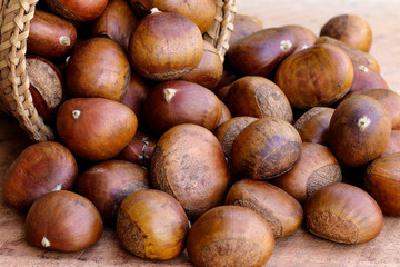 Ripe chestnuts in wicker basket on wooden background