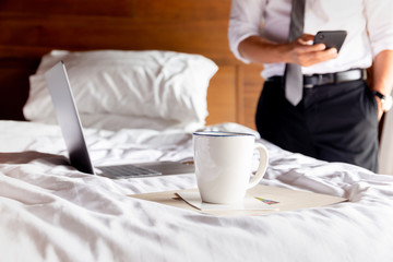 Coffee cup on table with businessman using cell phone and laptop in background.