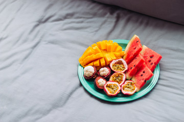 Obraz na płótnie Canvas Plate with tropical fruit in grey bed, breakfast