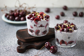 Chia pudding with cherry berries, natural yogurt, chia, pumpkin seeds in a glass on a grey surface. Front view. Healthy dessert,  super food 