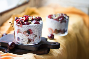 Chia pudding with cherry berries, natural yogurt, chia, pumpkin seeds in a glass on a yellow linen napkin. Front view. 