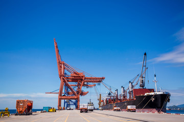 Fototapeta premium A cargo ship is loading with crane at Laemchabang port, Thailand. Logistics and transportation of Cargo ship with working crane bridge in blue sky background. Logistic import export and transport 