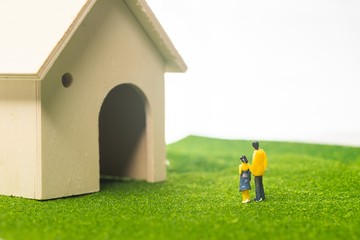 Miniature couple figures in front of a toy house, buying or owning a house concept