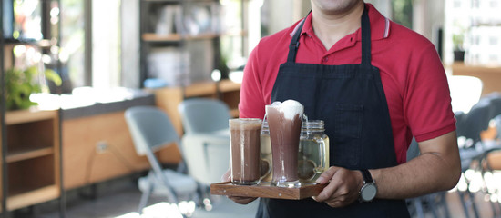 close up asian man barista smiling holding tray with coffee on it and cafe as background. cafe owner standing in restaurant