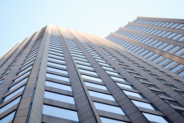 View looking up the side of a concrete and glass angular skyscraper in Boston with sun on the top