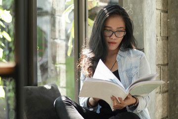 beautiful Asian women with glasses reading books by the window comfortably on a sunny day