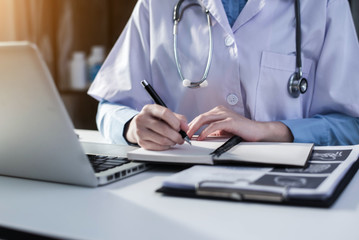 female in uniform of doctor using digital technology laptop for Output Device and writing a patient report on the office desk.