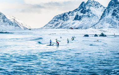 Surfers school outdoor practice on Lofoten Islands in Norway on snowy winter day. Water sports in cold weather.