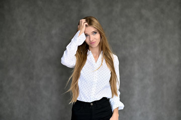 Portrait of a beautiful pretty girl student in a white shirt with long curly hair on a gray background. Beauty and brightness. Shows hands to the side, smiles with different emotions.