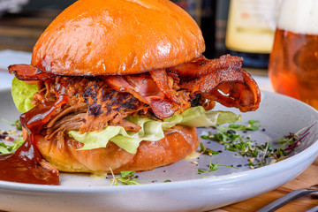 A Pulled Pork Burger with bacon, lettuce and barbecue sauce in a bead bun