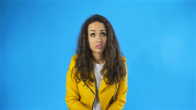 Portrait of serious woman in yellow jacket showing thumbs down sign to dislike in Studio with blue Background.