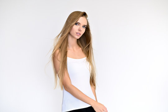 Portrait of a beautiful pretty girl student in a white T-shirt with long curly hair on a white background. Beauty and brightness. Shows hands to the side, smiles with different emotions.