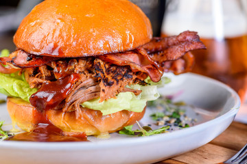 A Pulled Pork Burger with bacon, lettuce and barbecue sauce in a bead bun