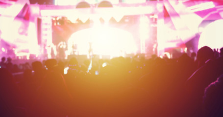 silhouettes of concert crowd at Rear view of festival crowd raising their hands on bright stage lights
