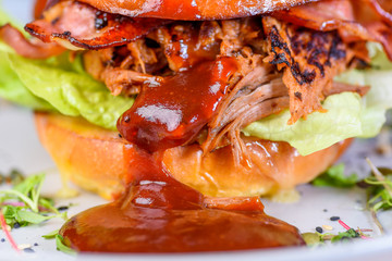 A Pulled Pork Burger with bacon, lettuce and barbecue sauce in a bead bun