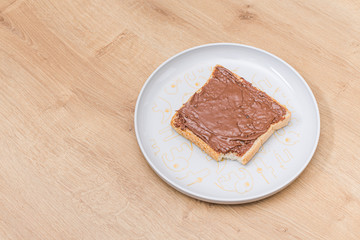 Chocolate nuts cream on a bread slice on a white plate