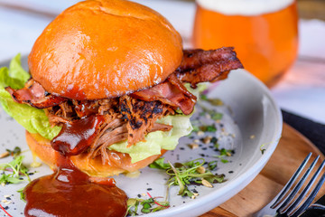 A Pulled Pork Burger with bacon, lettuce and barbecue sauce in a bead bun