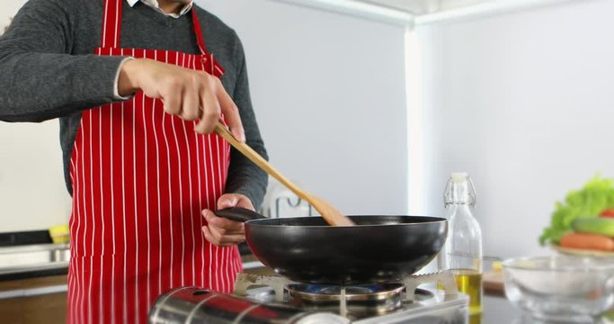 Tilting scene video of handsome Asian man in red apron fried french fries in a pan in the kitchen.