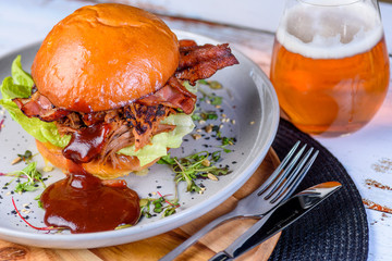 A Pulled Pork Burger with bacon, lettuce and barbecue sauce in a bead bun