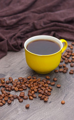 Yellow coffee cup and coffee beans on wooden background.