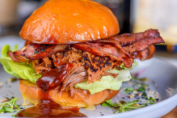 A Pulled Pork Burger with bacon, lettuce and barbecue sauce in a bead bun