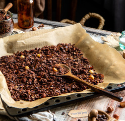 homemade baked chocolate granola with nuts, oat flakes on baking tray with parchment stands on grey wooden table