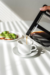 Avocado toasts and a cup of black coffee on a white table.
