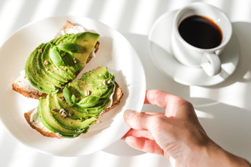 Avocado toasts and a cup of black coffee on a white table.