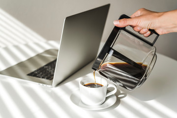 A laptop and a cup of black coffee on white table.