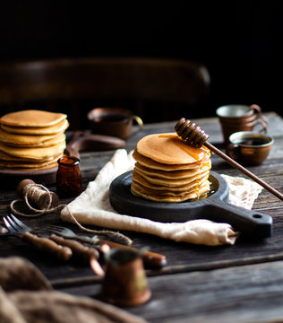 homemade two stacks of pancakes on wooden boards with pouring honey and honey stick