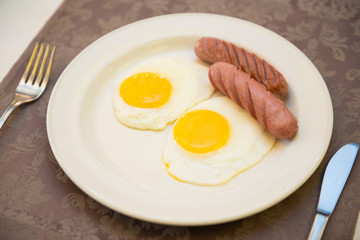Fried eggs with sausages in a plate on the table.