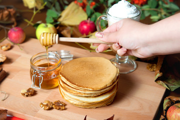 A stack of pancakes is poured with honey on a decorated table. Restaurant dishes.