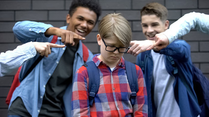 Evil schoolchildren pointing fingers at junior boy, mocking nerd, bullying - obrazy, fototapety, plakaty