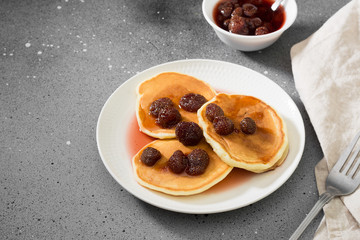 Pancakes with strawberry jam on a white plate. Gray background