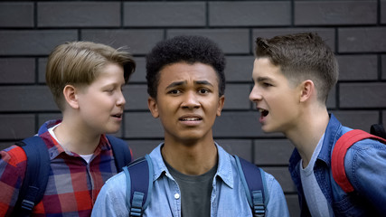 Cruel students teasing black boy face-to-face, telling insults, racial bullying