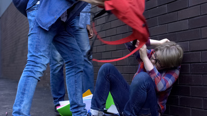 Schoolchildren throwing things out of backpack on boy head, bullying at school