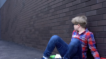 Abused boy sitting helpless near wall, depressed victim of bullying intimidation