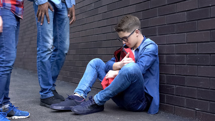 Teen boy leaning against wall, scared of bully students, intimidation at school